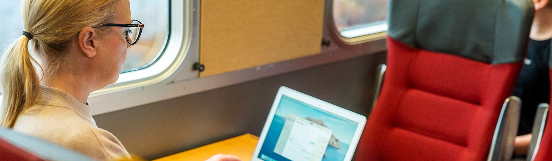 En kvinna sitter med sin dator ombord på tåget och jobbar.
