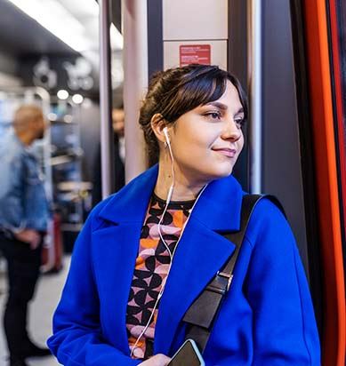 En tjej i blå kappa står vid Öresundstågets mittdörrar och tittar ut.