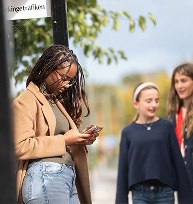 Kvinna tittar ner i sin telefon i väntan på bussen.