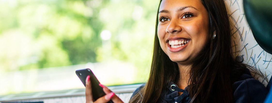 En ung tjej sitter ombord på ett Öresundståg och håller i en mobiltelefon och ler.