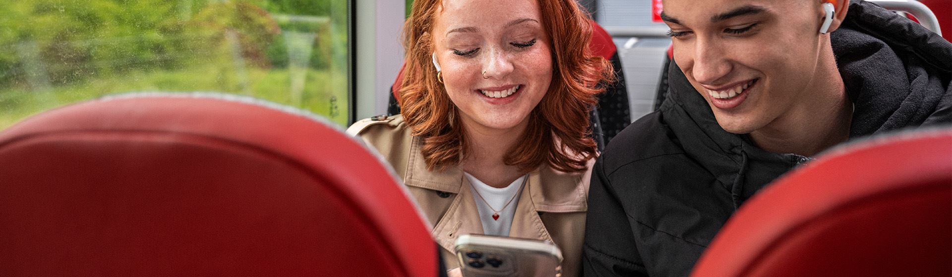 Två personer sitter ombord på en buss och tittar i mobiltelefonen.