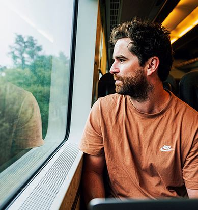 En kille sitter ombord ett tåg och tittar ut genom fönstret.