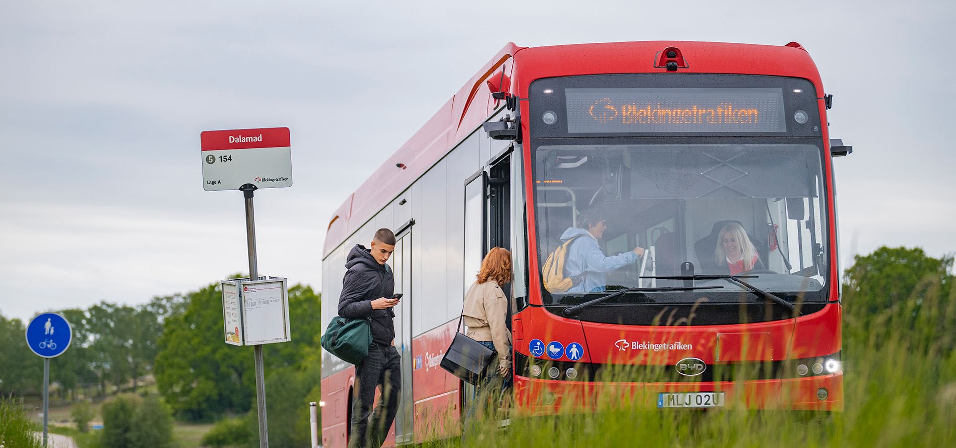 Fem personer väntar på bussen vid en busshållplats.