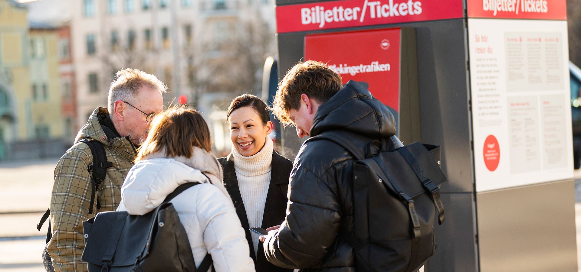 Fem personer väntar på bussen vid en busshållplats.