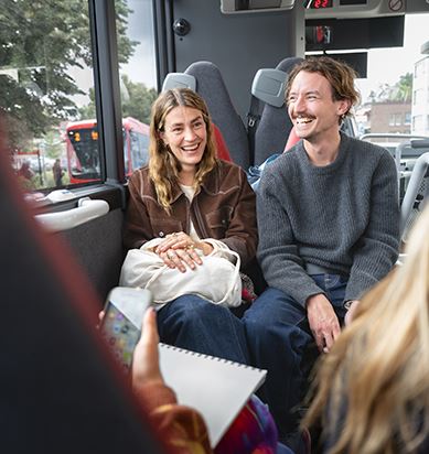 Två resenärer sitter på en buss och skrattar. 