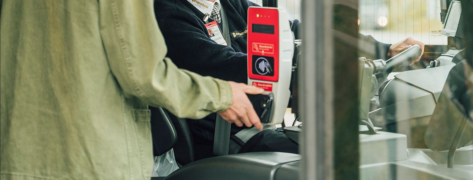 En resenär håller en smartphone mot en röd biljettläsare på bussen.