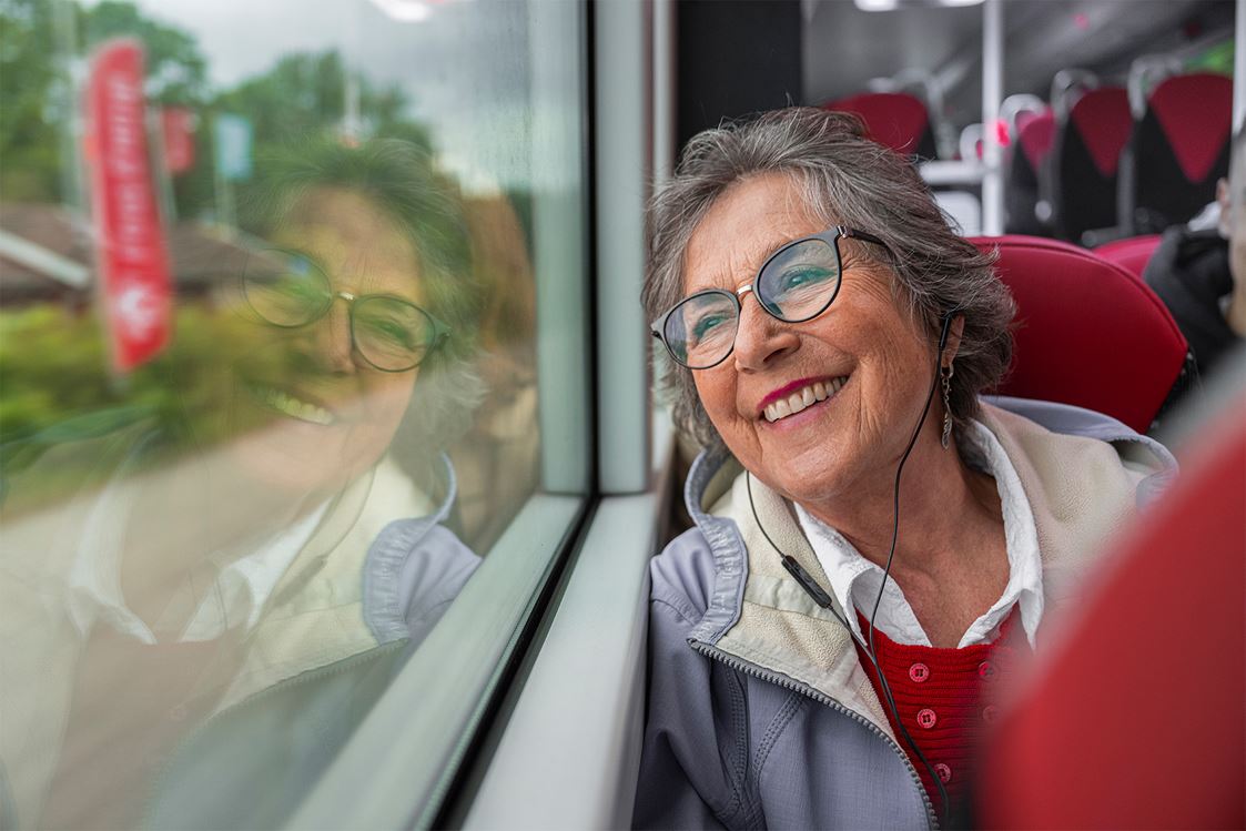 En leende kvinna sitter och tittar ut genom fönstret ombord på en buss.