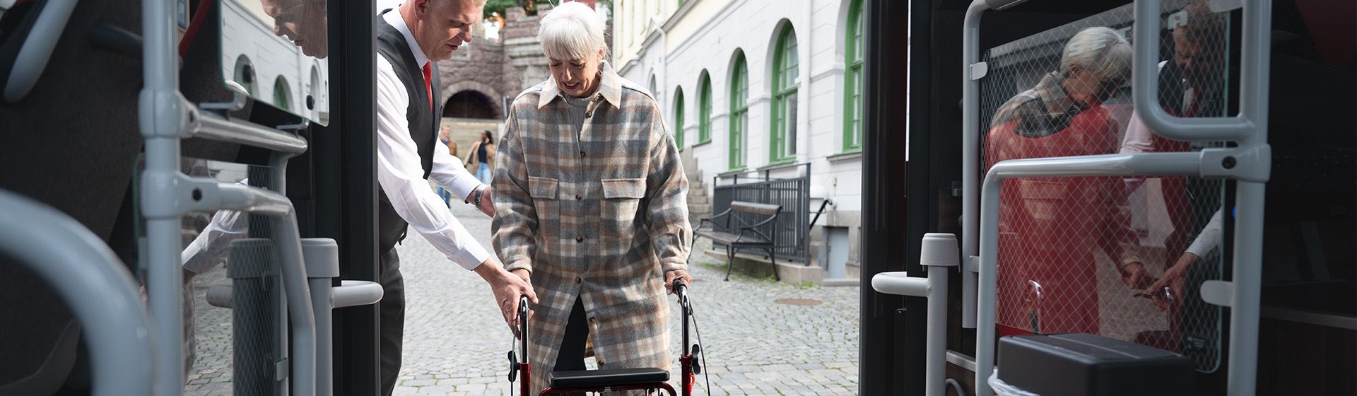 En förare hjälper en kvinna med rullator att stiga ombord på bussen.