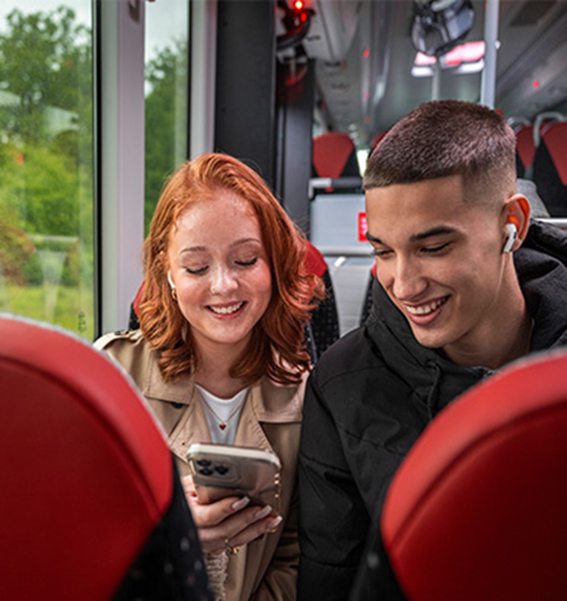 Två ungdomar åker buss och kollar ner i en telefon.