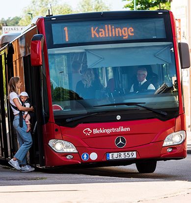 Kvinna med barn i bärsele kliver på buss linje 1 till Kallinge.