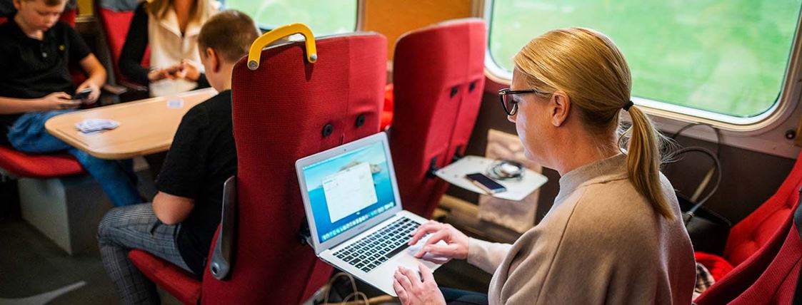 En kvinna sitter med sin dator och jobbar ombord på ett Krösatåg.