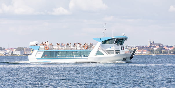 Båten M/F Ljungskär kör i skärgården. Flera personer står uppe på soldäck.