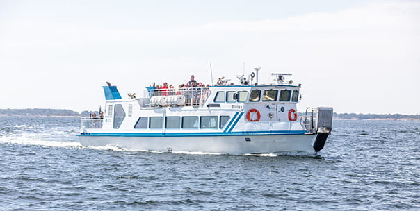 Båten M/F Wittus kör i skärgården. Passagerare står uppe på soldäck.