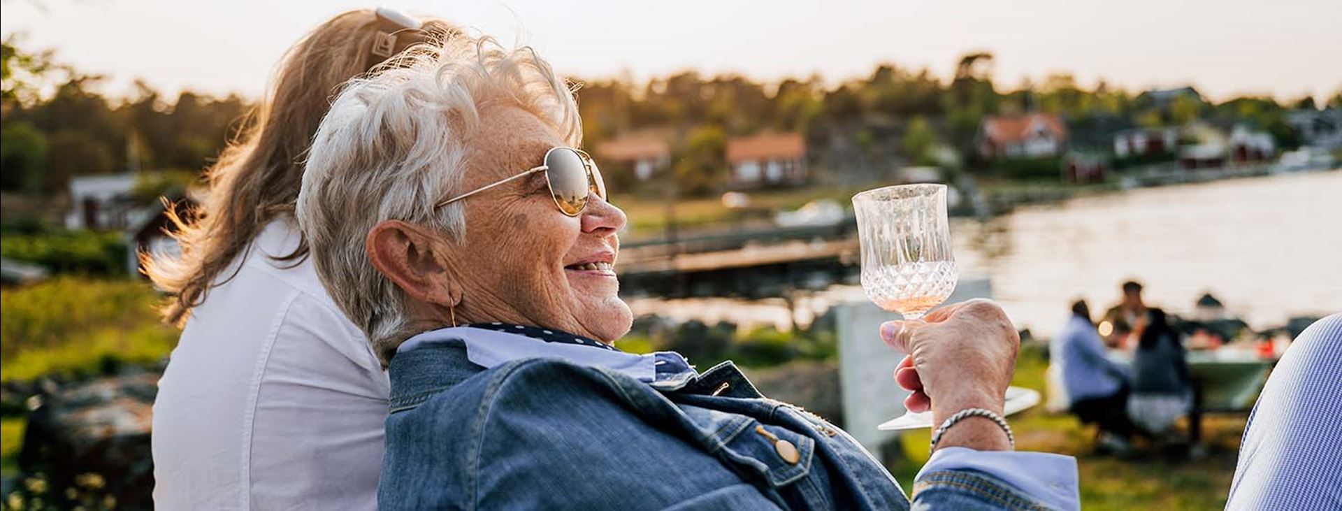 En äldre dam med solglasögon håller i ett glas med dryck.