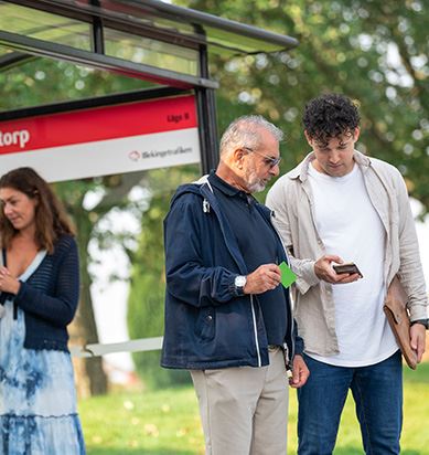 Tre personer står vid en busshållplats.