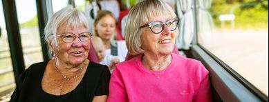 Två äldre damer sitter ombord på en buss. Bakom sitter en kvinna med ett barn.