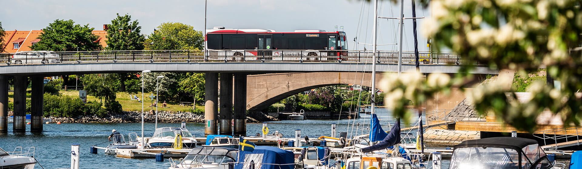 En buss kör över en bro och i förgrunden syns båtar ligga i vattnet.