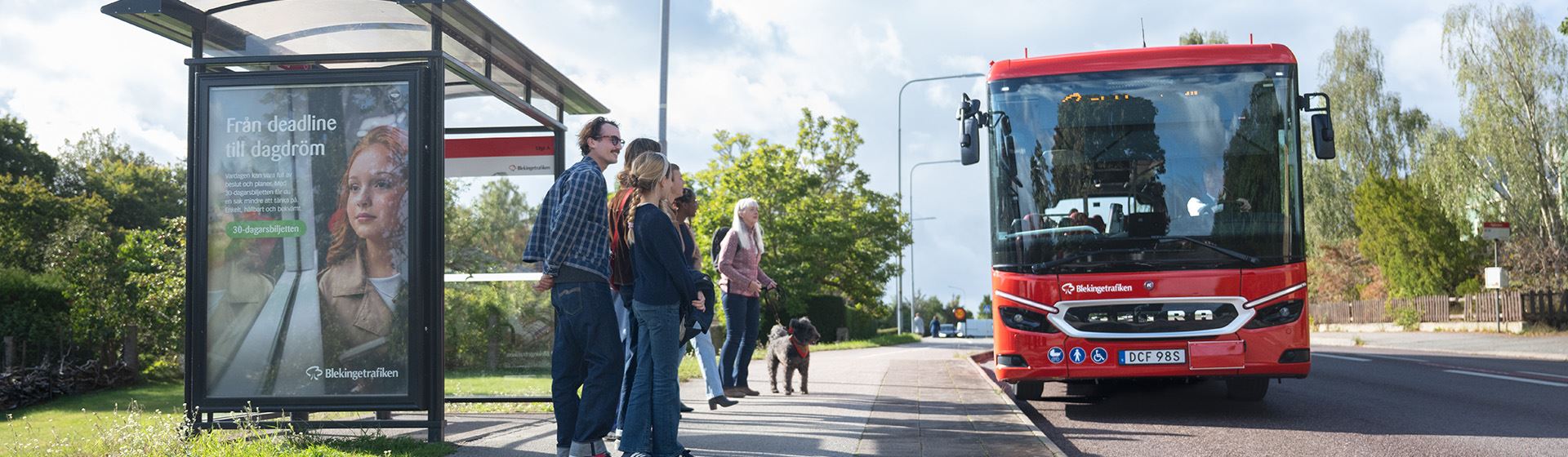 En buss kör fram till en hållplats där det väntar resenärer.